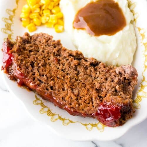 meatloaf on a white platter with mashed potatoes and corn.